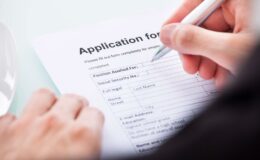 A person holding a pen is writing on an application form.