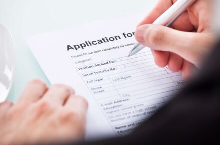 A person holding a pen is writing on an application form.