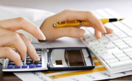 A hand pressing a key on a calculator while also holding a pen in the other.