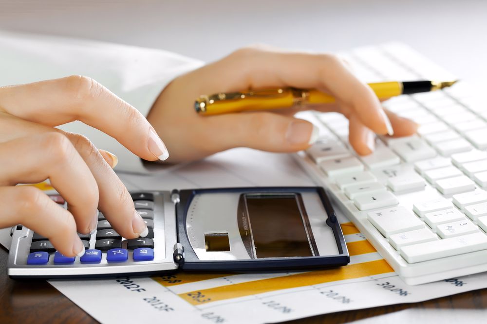 A hand pressing a key on a calculator while also holding a pen in the other.