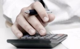 A hand holding a pen while using a calculator.