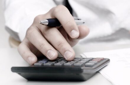 A hand holding a pen while using a calculator.