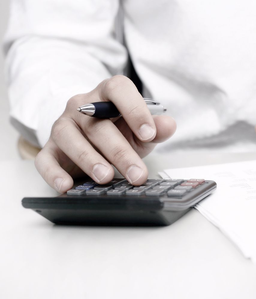 A hand holding a pen while using a calculator.